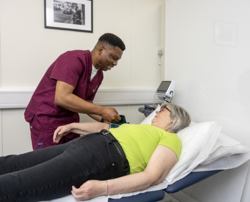 A woman is lying on a clinical bed having her blood pressure taken by a male nurse