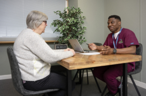 A woman is talking to a male nurse. They are sitting at a table opposite each other