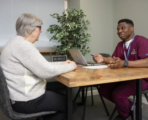 A woman is talking to a male nurse. They are sitting at a table opposite each other