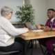 A woman is talking to a male nurse. They are sitting at a table opposite each other