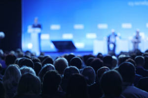 Photo of an audience watching a conference with people on stage